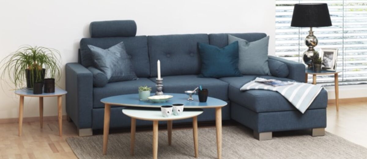 Et blødt, grovstrikket uldtæppe draperet afslappet over armlænet på en moderne beige sofa – tæppe til sofa i nordisk stil.