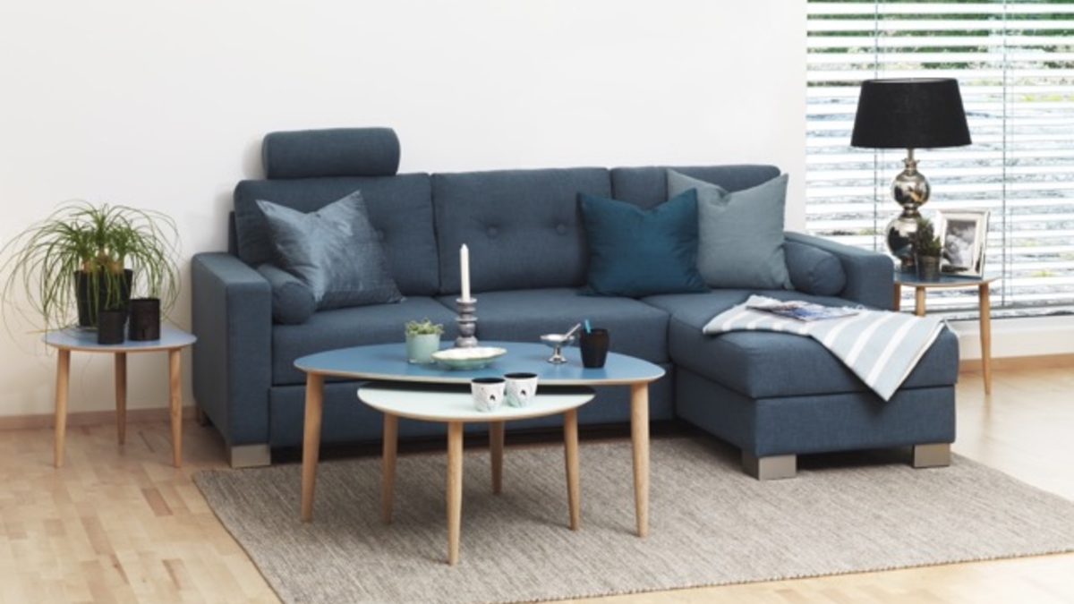 Et blødt, grovstrikket uldtæppe draperet afslappet over armlænet på en moderne beige sofa – tæppe til sofa i nordisk stil.